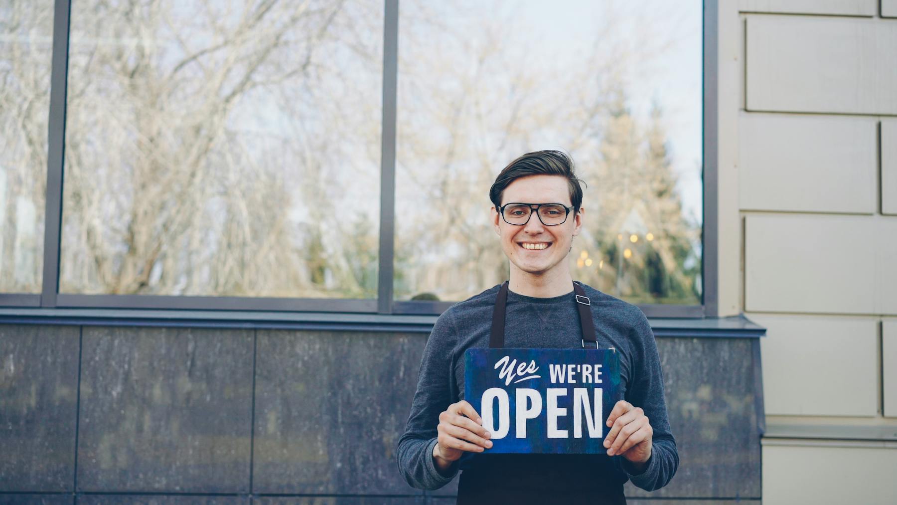 Small business owner smiling while holding an open sign outside a storefront
