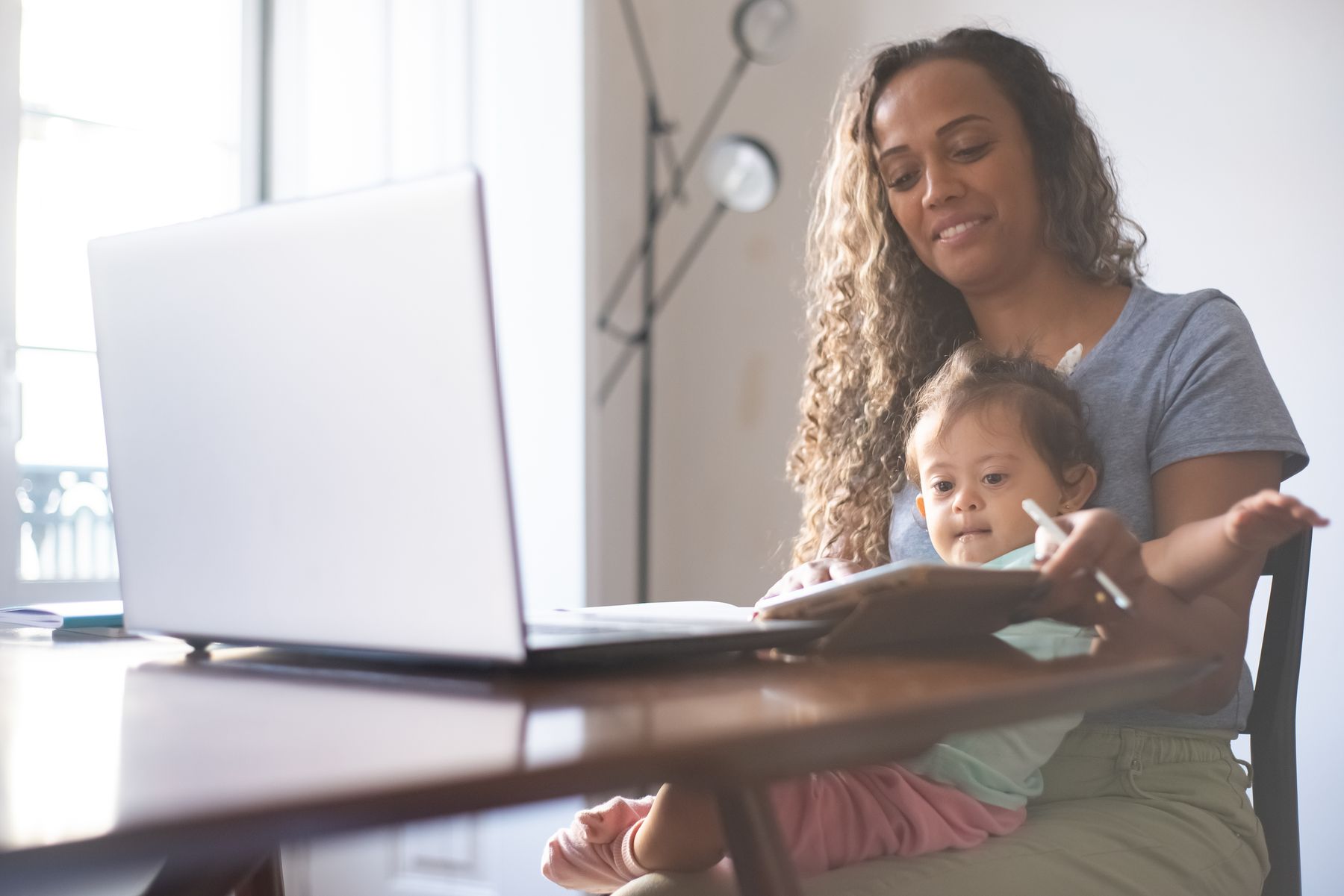 Working parent handling client work on a laptop while a child sits nearby