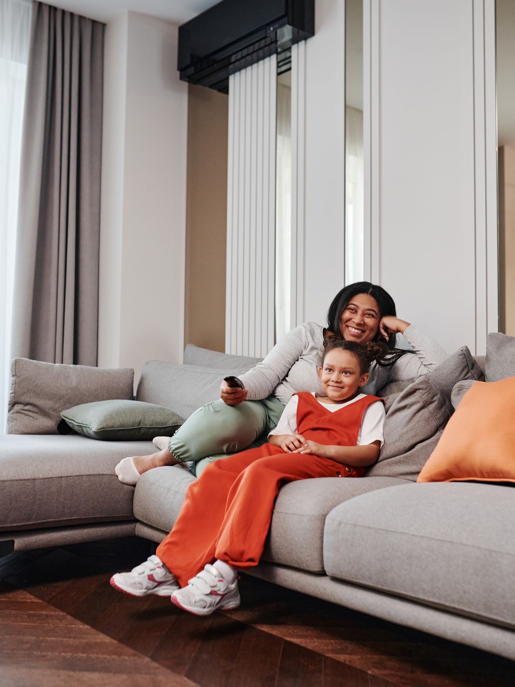 Mother and daughter relaxing on the sofa beneath a quietly running air conditioner